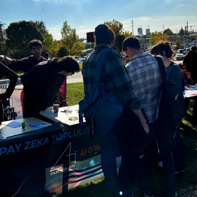 Standın önünde toplanmış, masaya bakan öğrenciler.